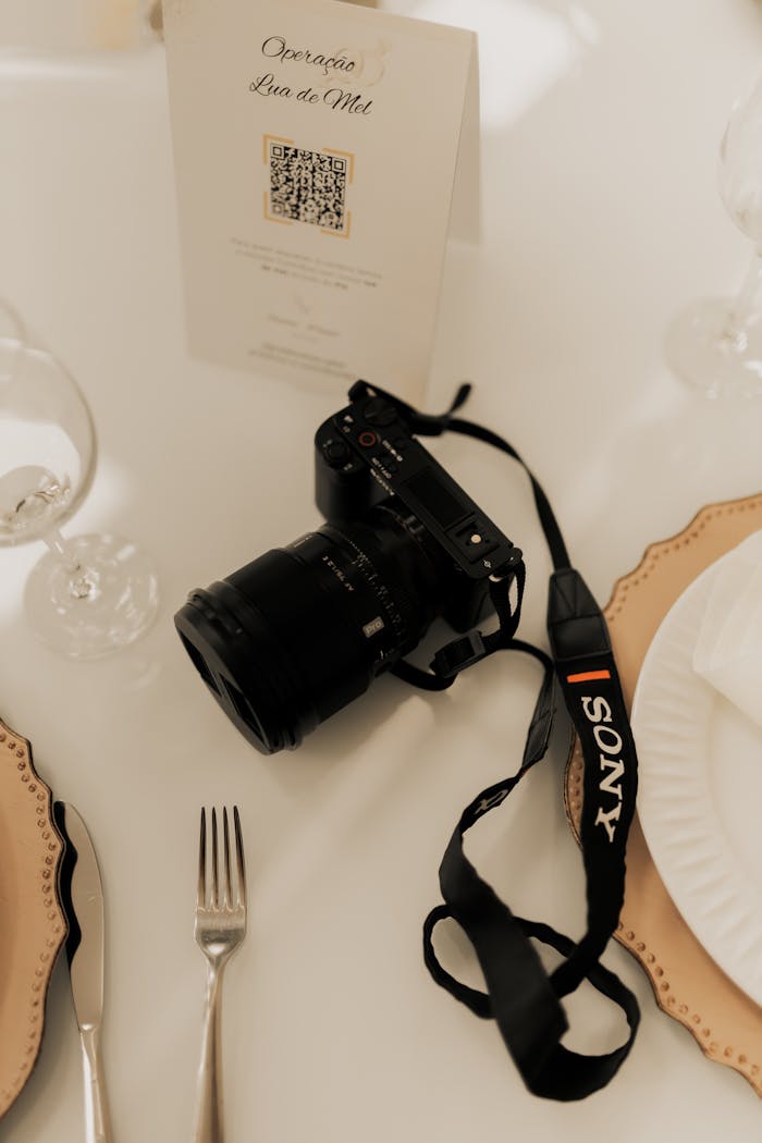 A DSLR camera on an elegant dining table, surrounded by fine dining utensils.